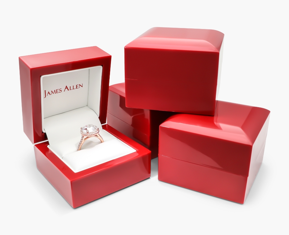 Four James Allen classic red boxes. One of them is open showing a rose gold pavé halo diamond engagement ring.